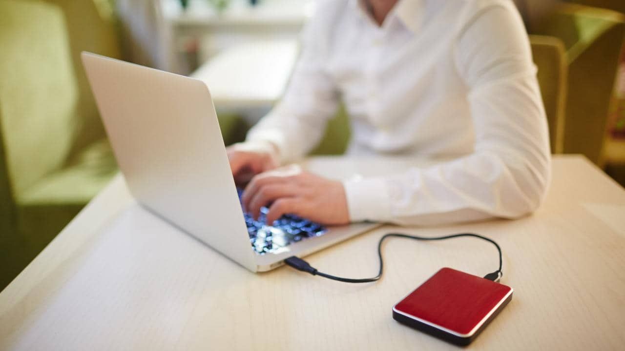 Imagem de um homem em frente ao computador, com um HD externo conectado ao dispositivo.